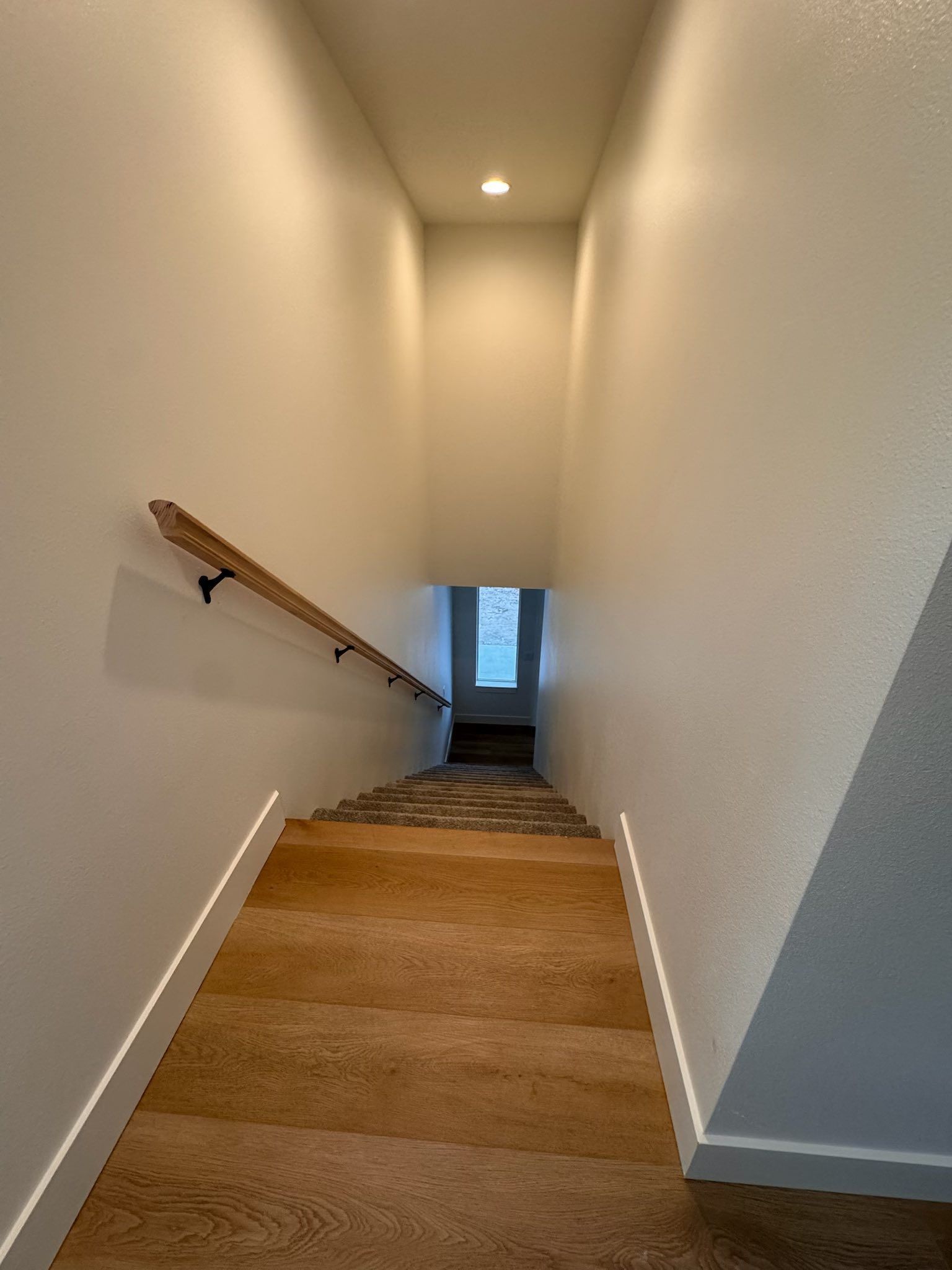 Staircase with wooden steps and handrail, descending into a brightly lit space with window at the bottom.