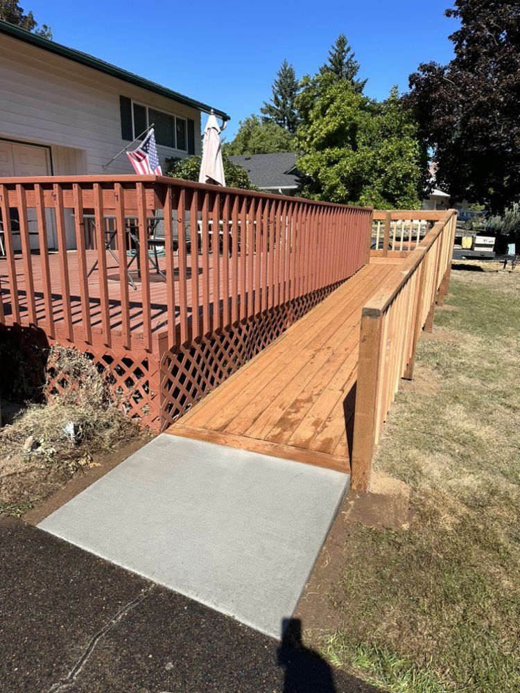 Wooden ramp with railings leading from a deck to a concrete walkway. Brown and tan wood with a blue sky.