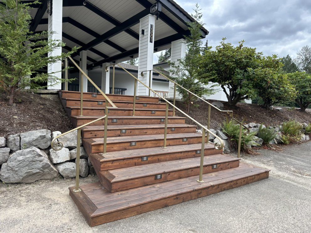 Wooden steps with brass handrails lead up to a white building with black accents.