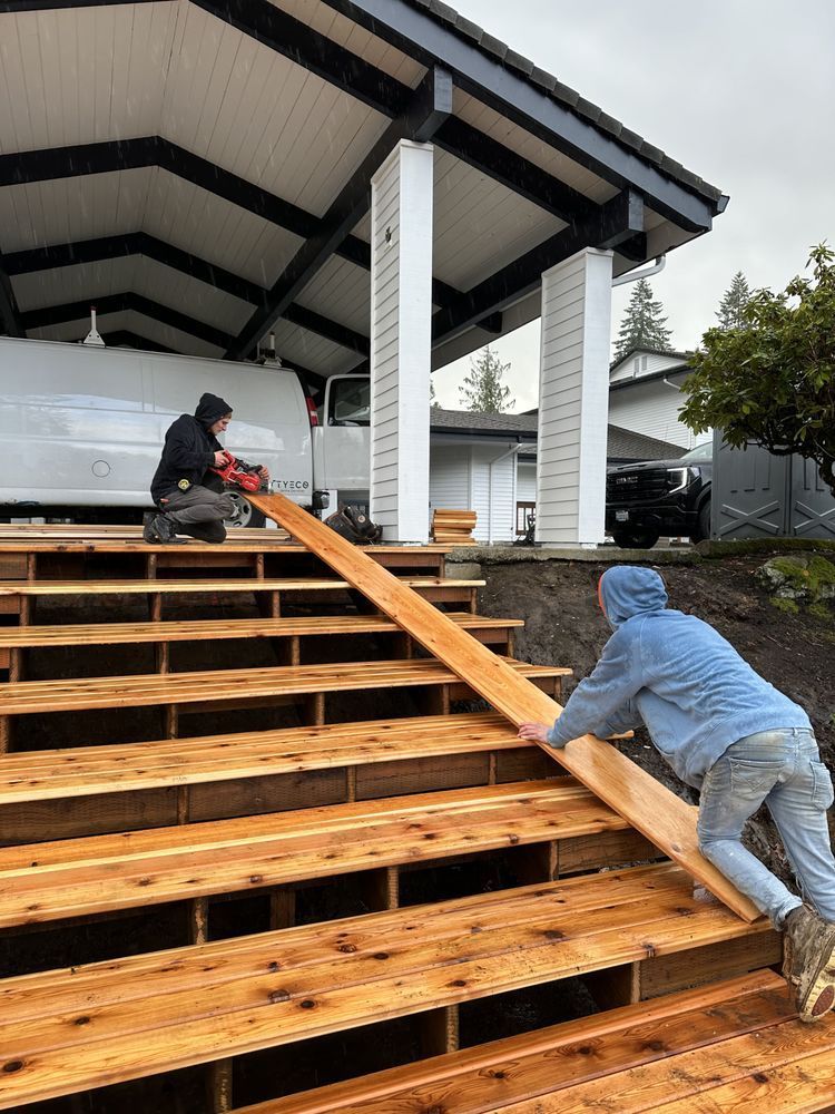 Two workers installing wooden steps on a house porch, one using a saw, the other carrying a board.