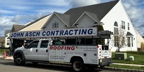 White truck with John Asch Contracting sign parked in front of a house, advertising roofing services.