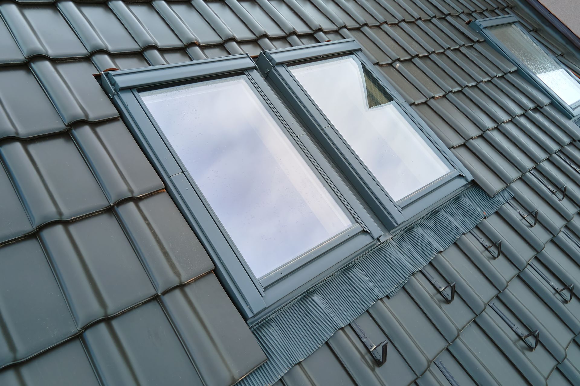 Skylights on a tiled roof. One window open, gray tiles, and flashing visible.