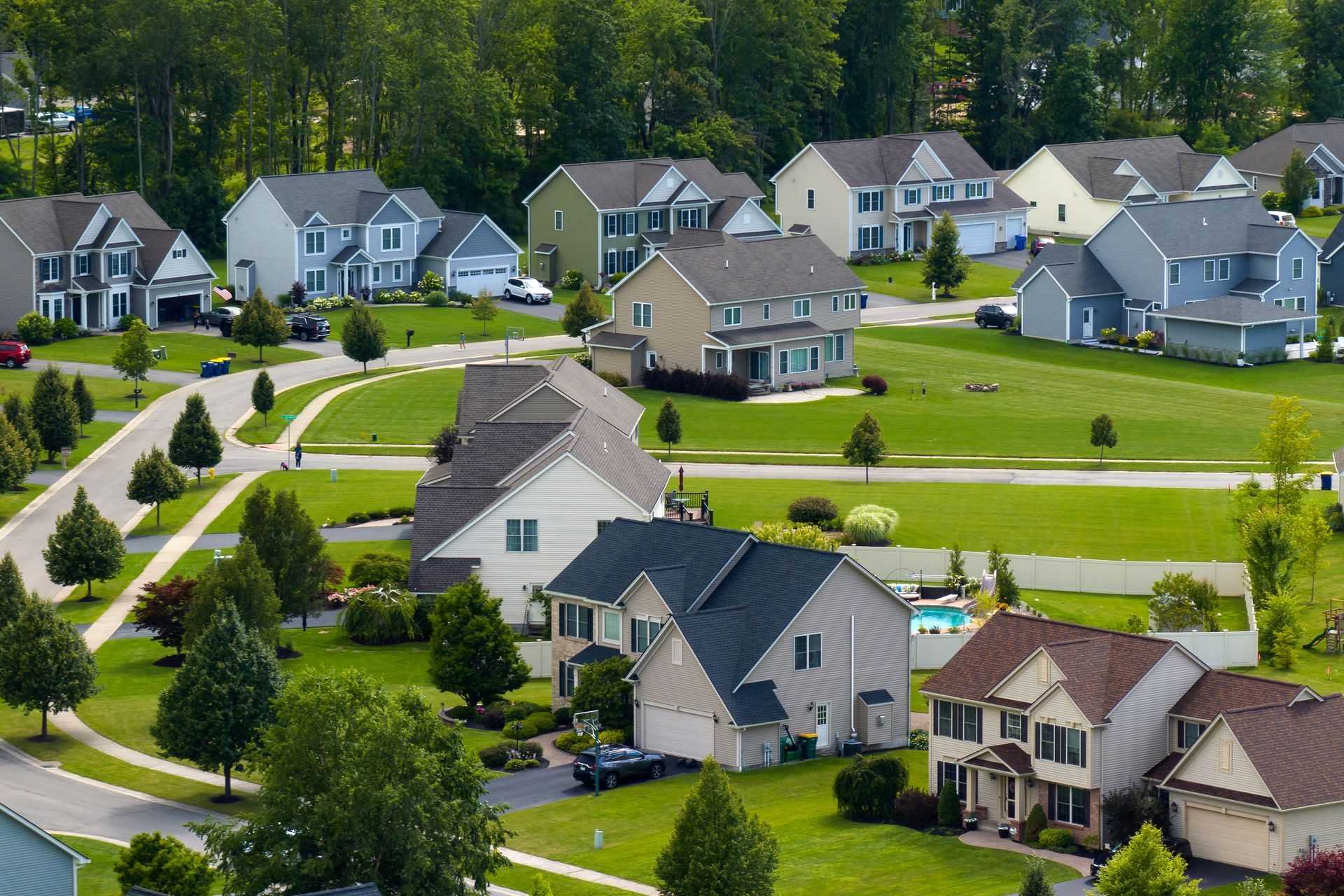 Suburban neighborhood with houses, green lawns, and trees under a sunny sky.