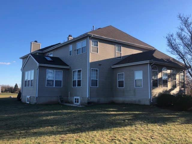 Two workers installing black metal roof panels on a wooden house.