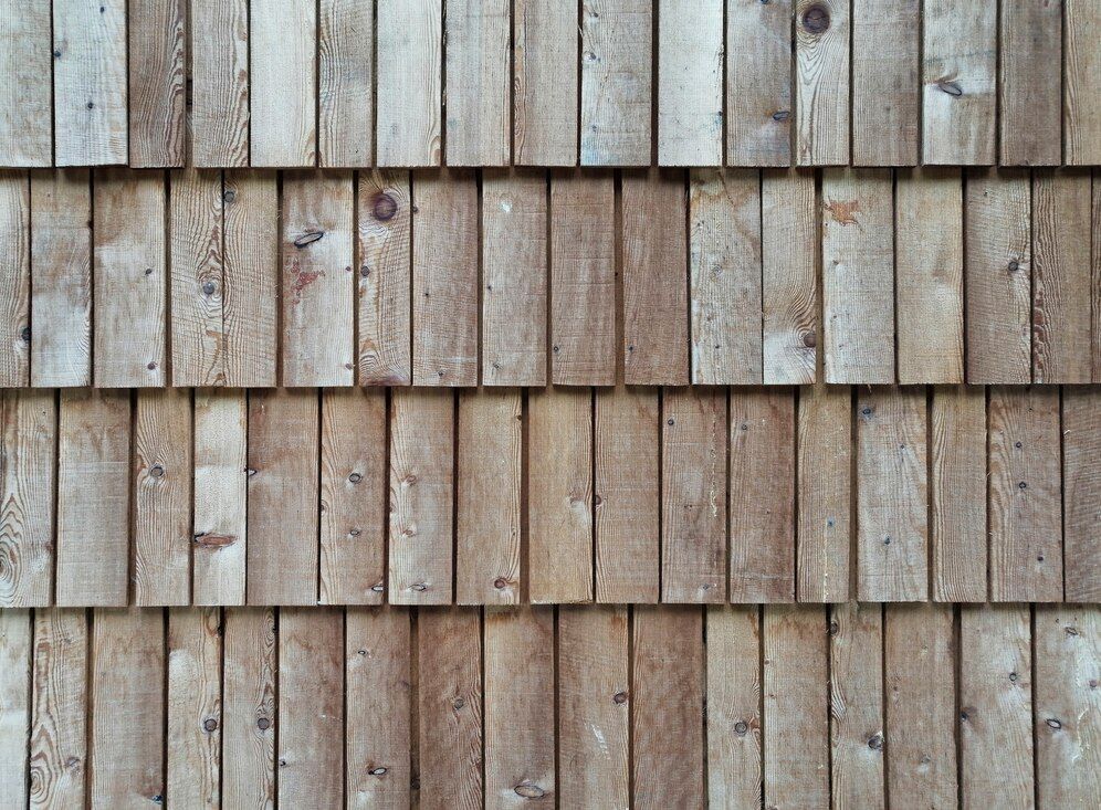 Wooden shingle siding, natural wood color, textured surface.