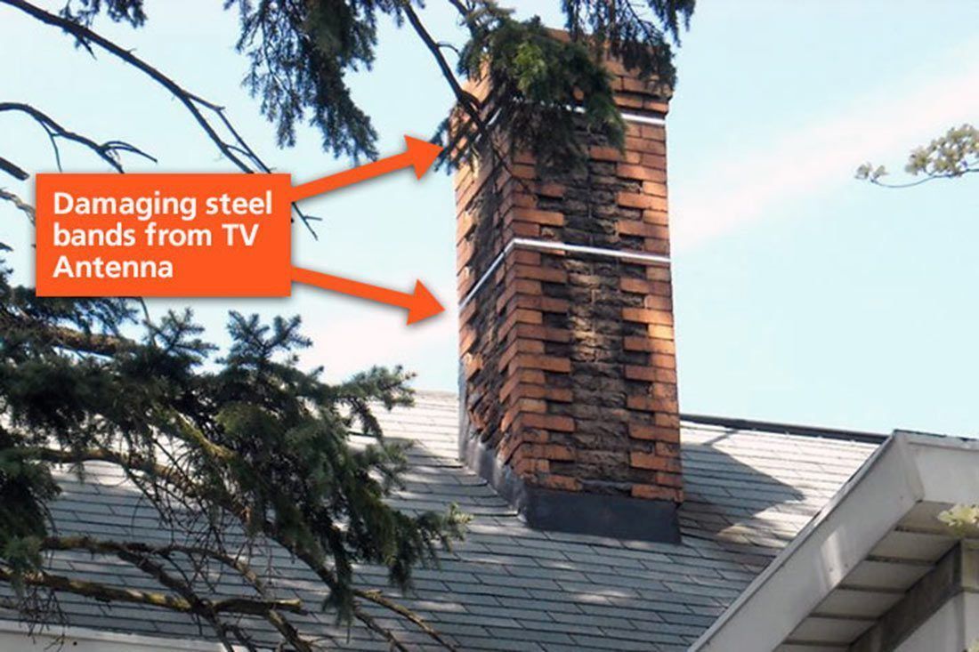 Chimney with steel bands from a TV antenna; tree branches in the foreground.