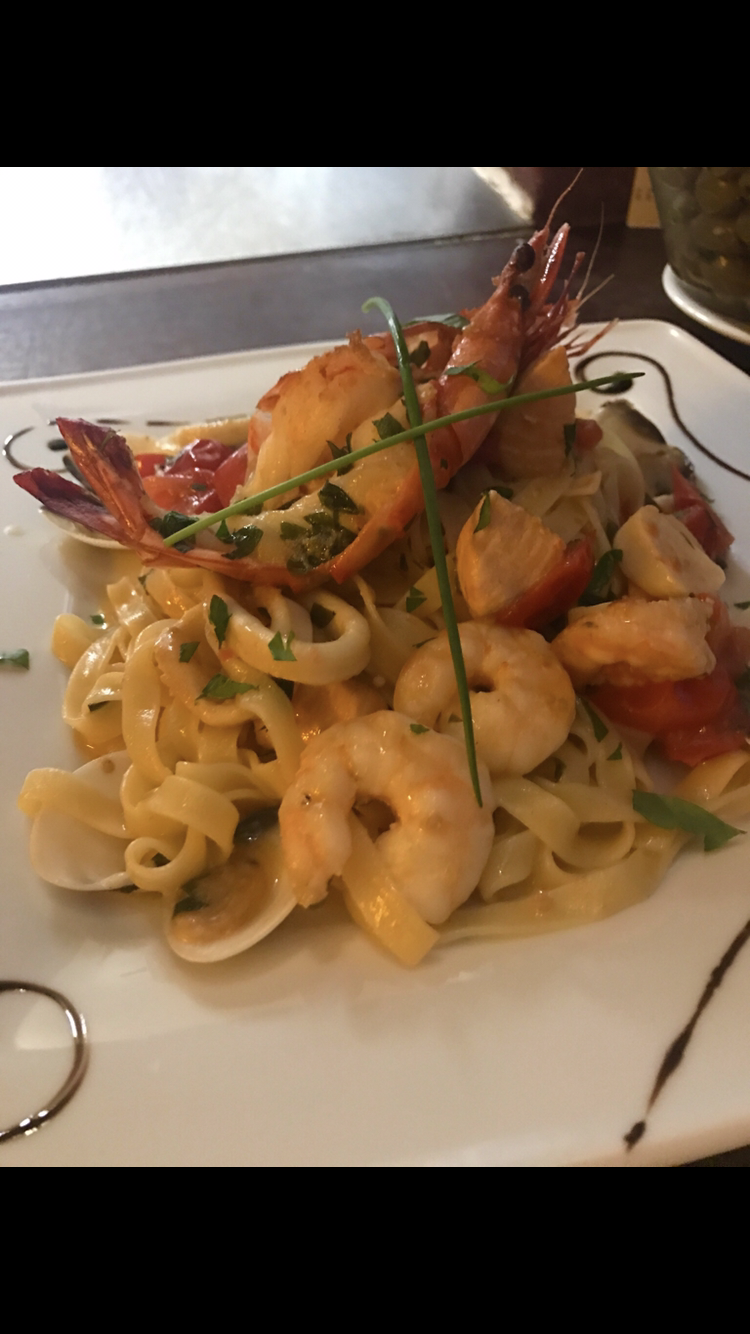 Ein weißer Teller mit Nudeln und Garnelen auf einem Tisch.