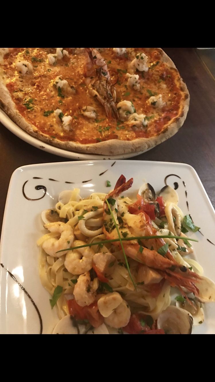 Auf einem Tisch stehen eine Pizza und ein Teller Pasta.