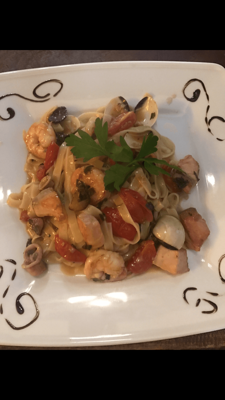 Ein weißer Teller mit Nudeln, Garnelen, Tomaten und Petersilie.