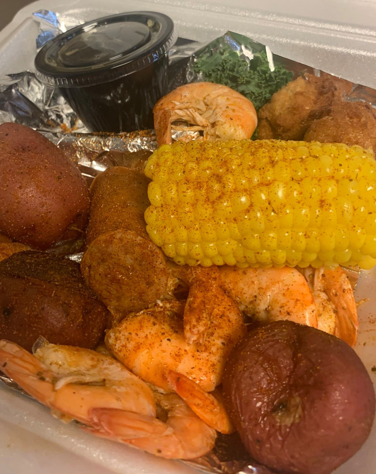 A tray of food with shrimp , corn on the cob , potatoes , and spinach.