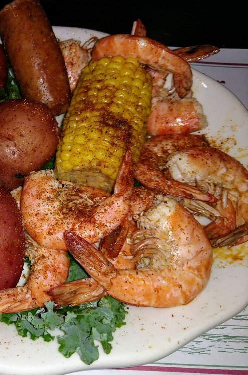 A white plate topped with shrimp , corn on the cob , potatoes and sausage.