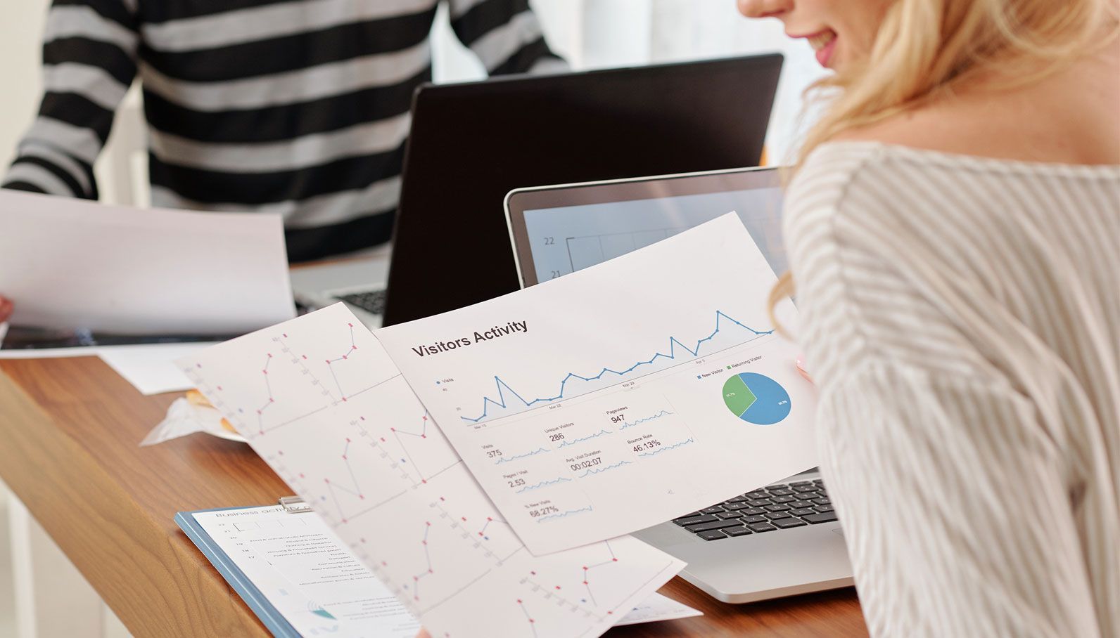 Two people reviewing charts and a laptop at a desk.