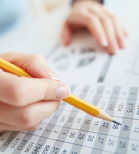 Person's hand pointing at numbers on a document with a yellow pencil.