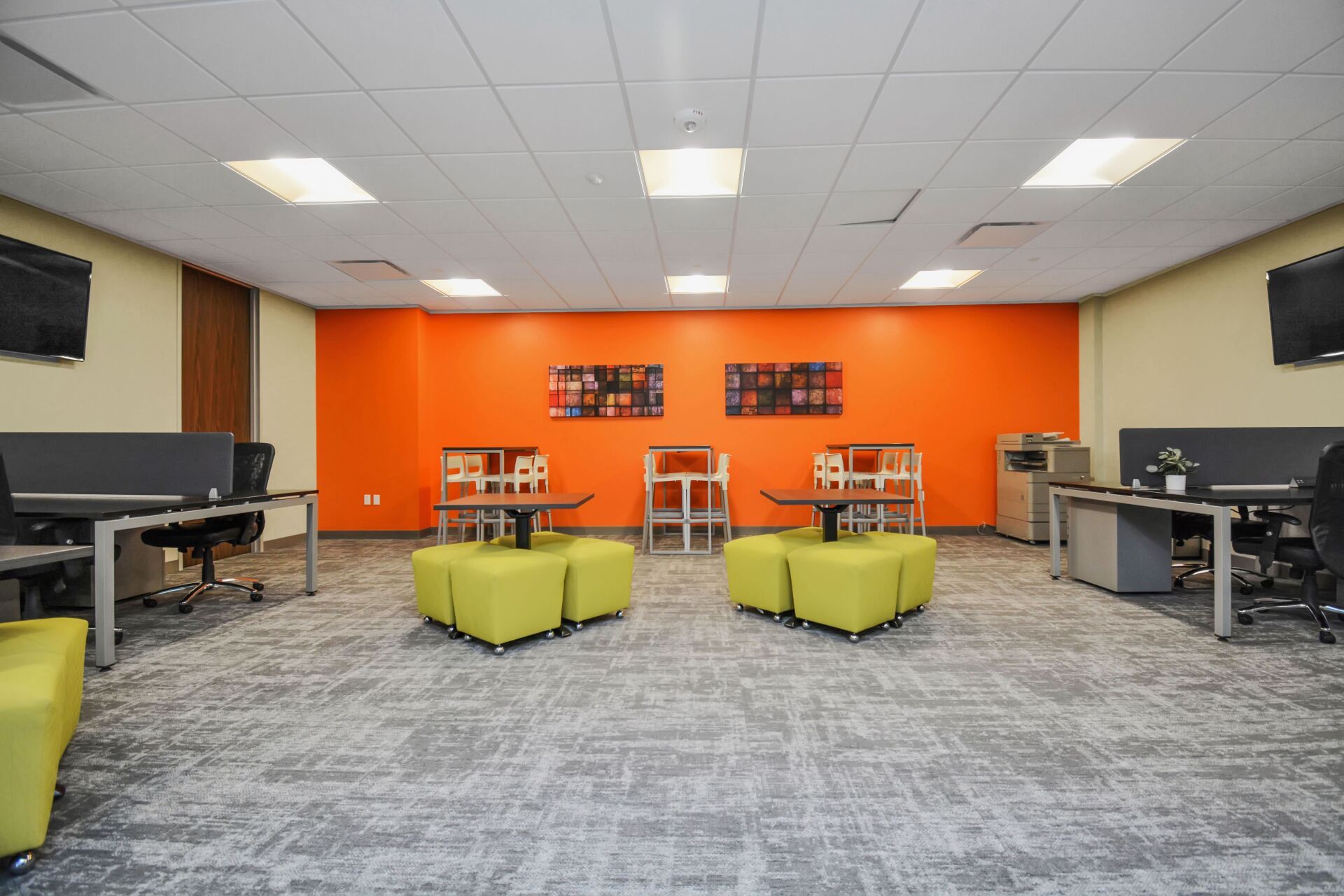 A large room with tables , chairs , ottomans and a orange wall.