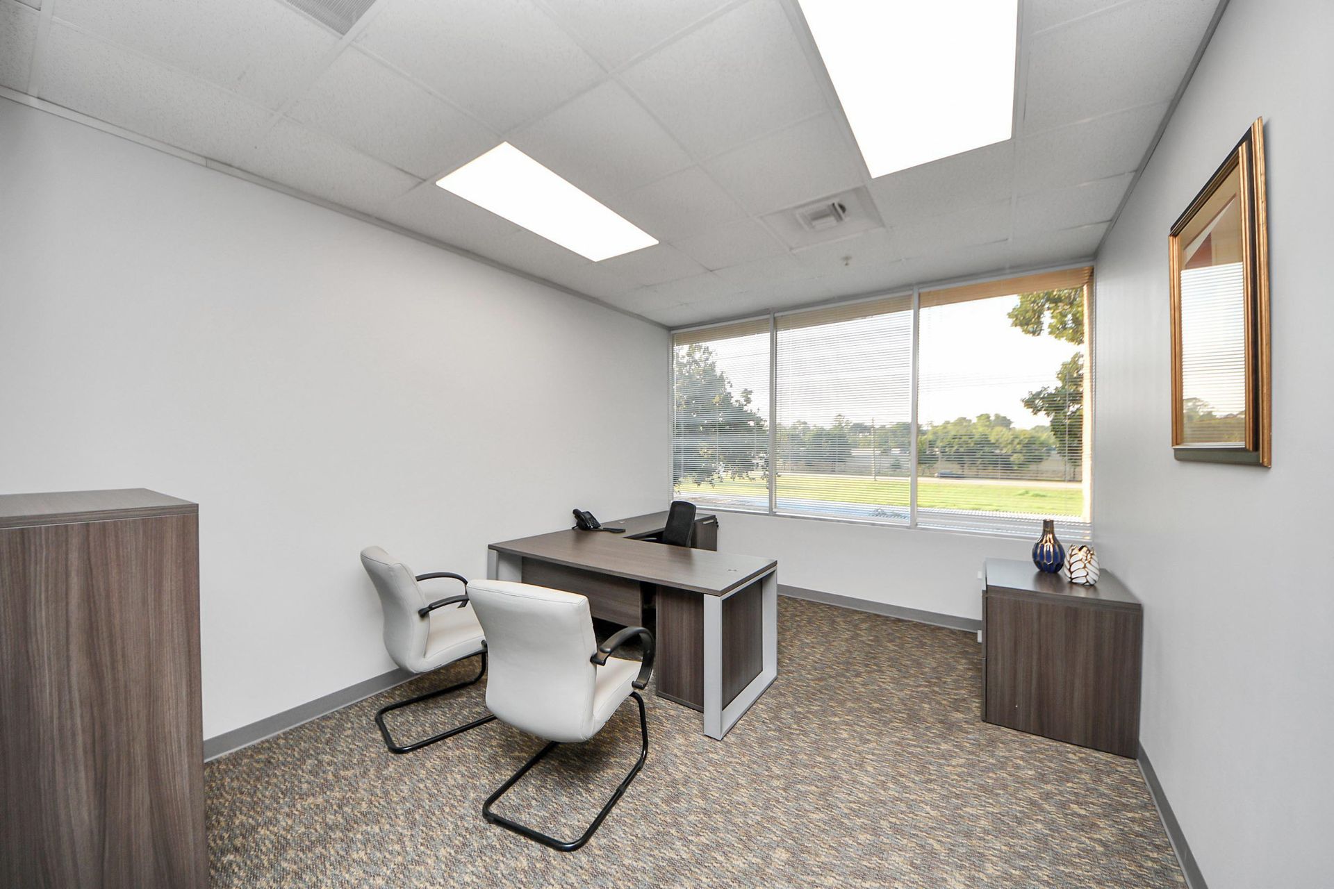 A small office with a desk , chairs and a window.