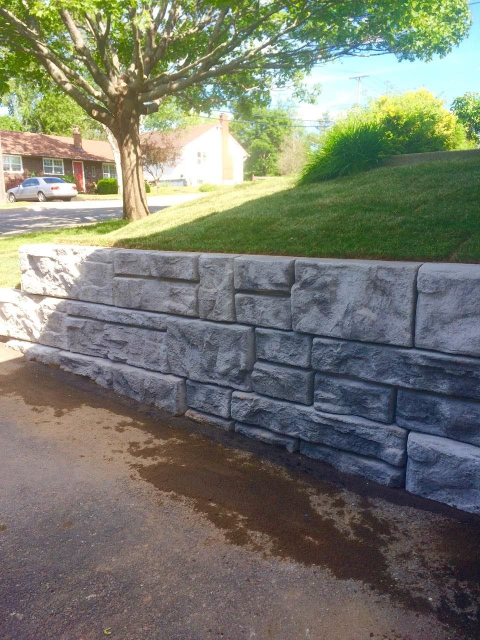 A stone wall is sitting on the side of a road next to a tree.