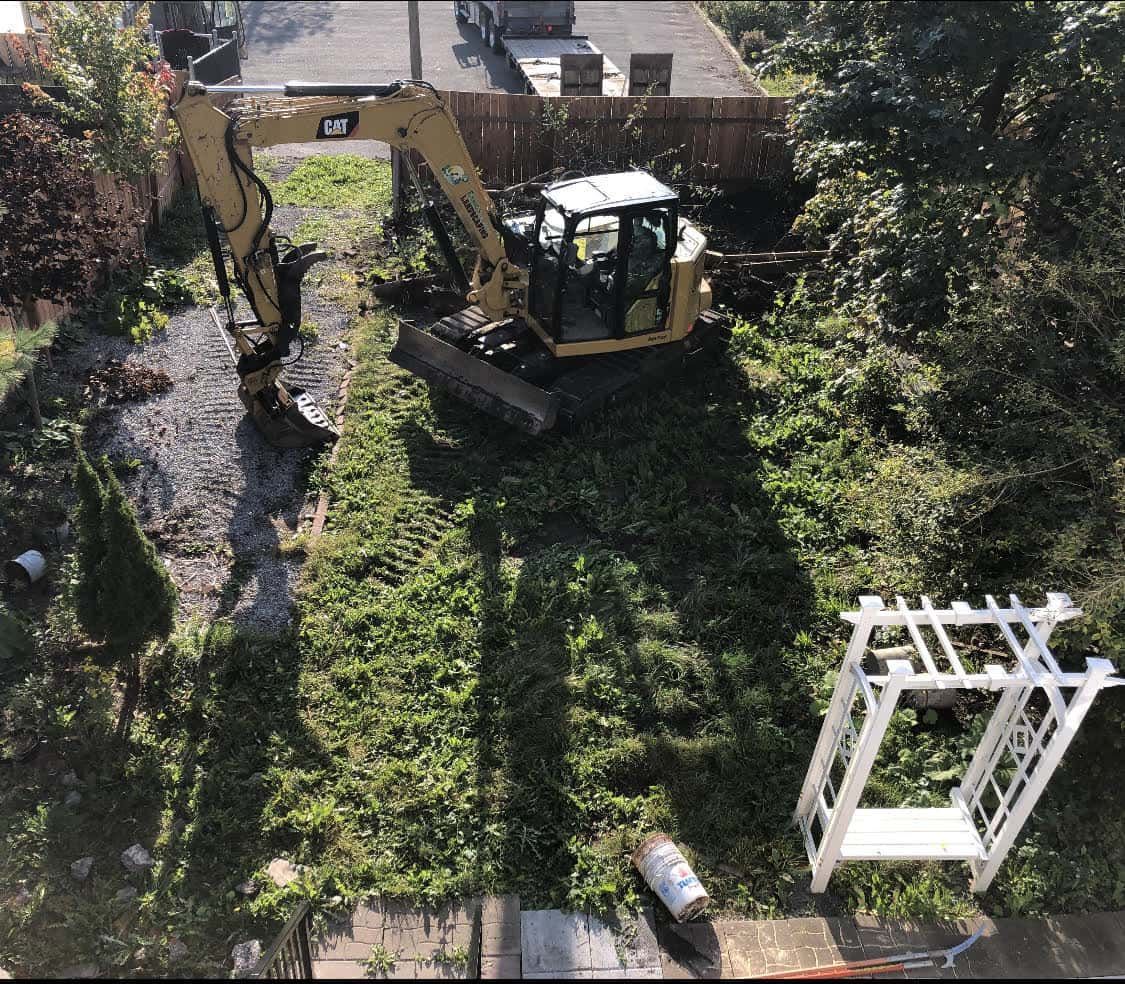 A cat excavator is digging a hole in a yard.