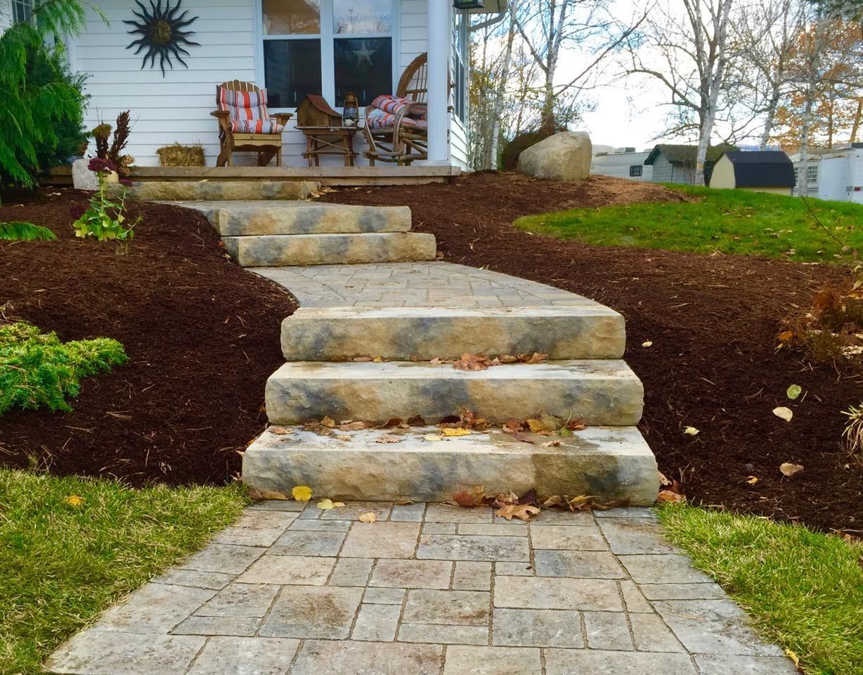 A stone walkway leading to a porch with rocking chairs
