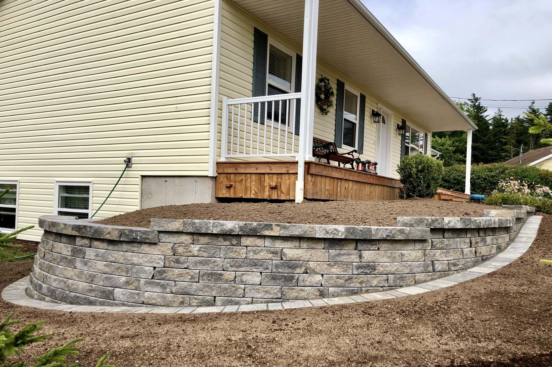 A house with a porch and a stone wall in front of it.