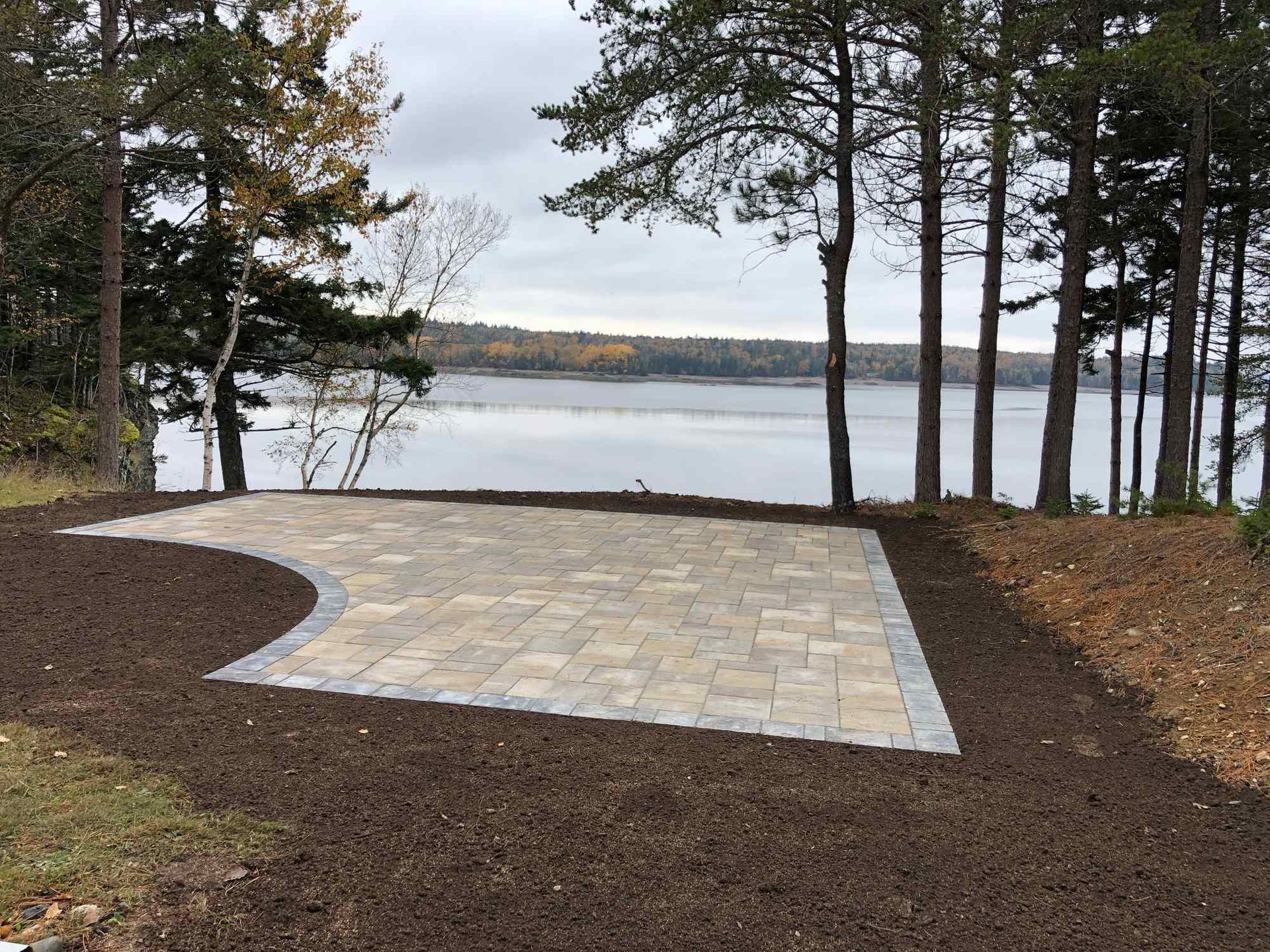 A brick driveway leading to a lake surrounded by trees.