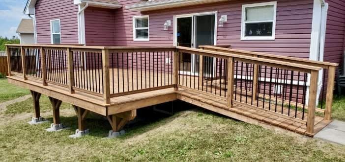 A wooden deck with a ramp attached to it is in front of a pink house.