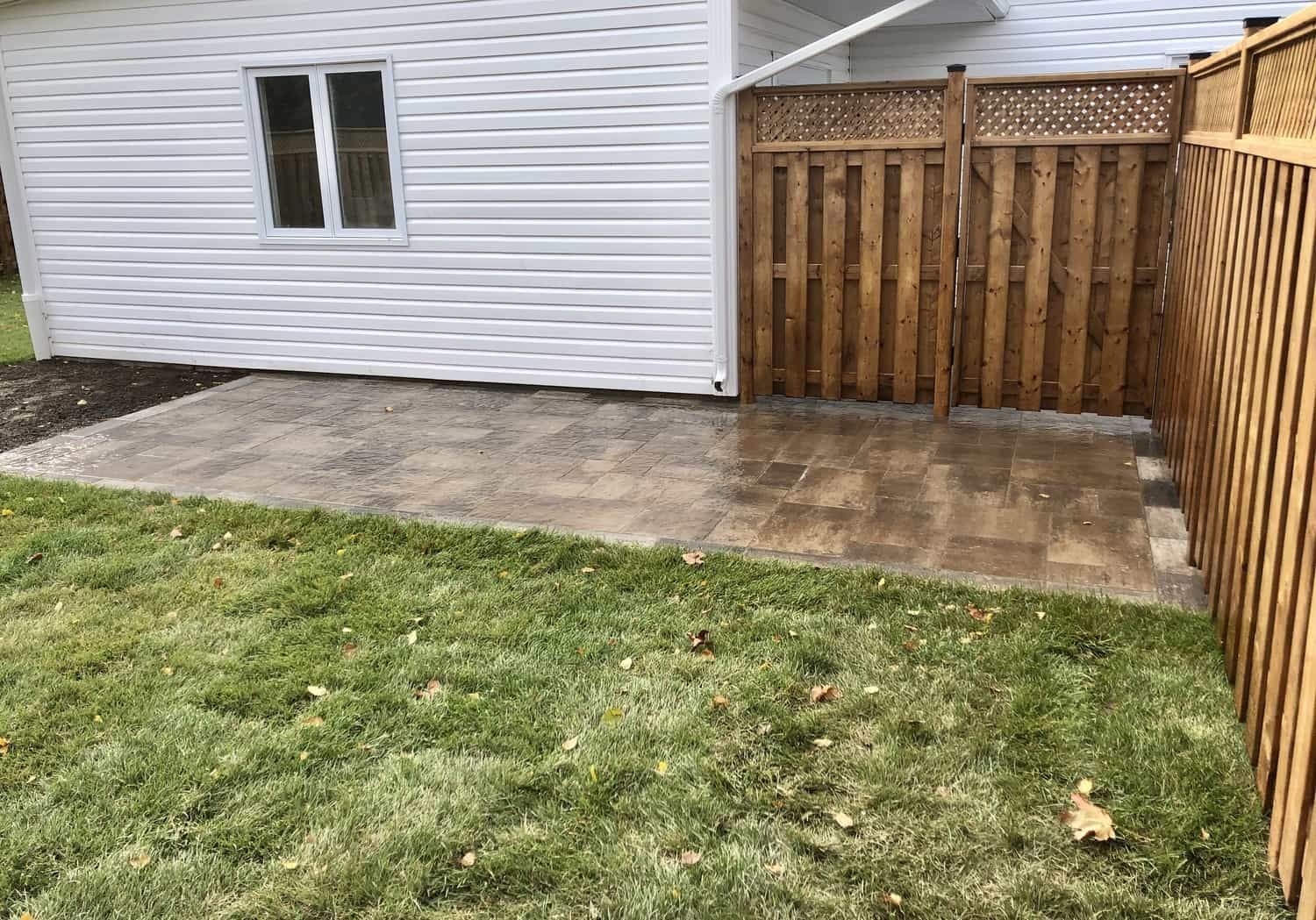 A backyard with a wooden fence and a patio in front of a house.