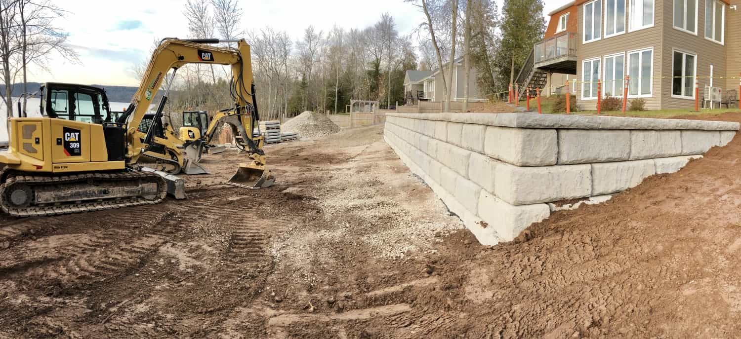 A construction site with a large pile of dirt and a house in the background.