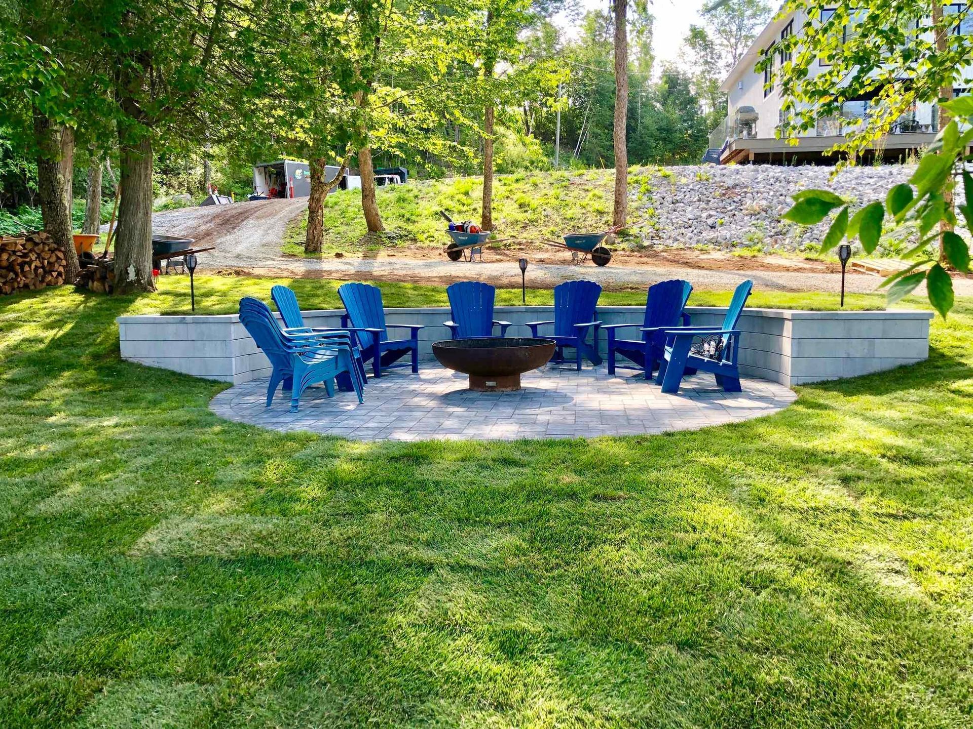 A fire pit surrounded by blue chairs in a lush green yard.
