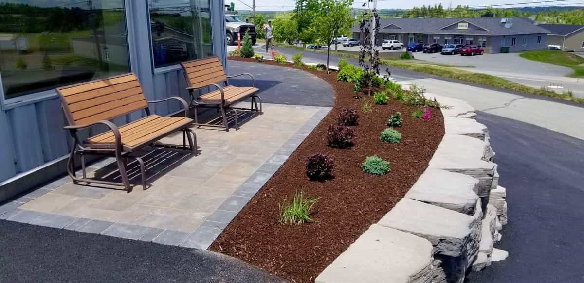 A patio with two benches and a rock wall in front of a building.