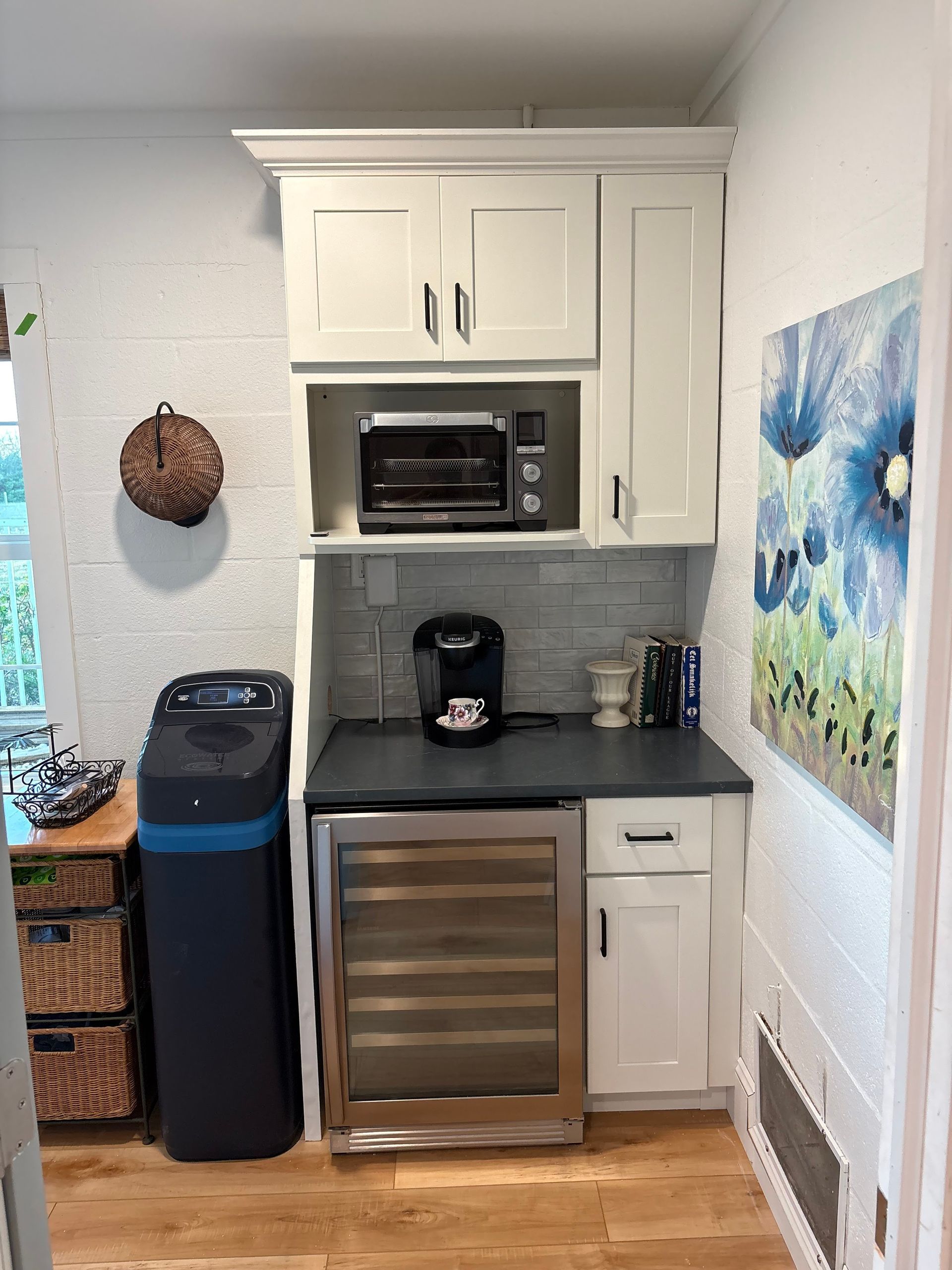 A kitchen with white cabinets , a stainless steel refrigerator , a coffee maker , and a trash can.