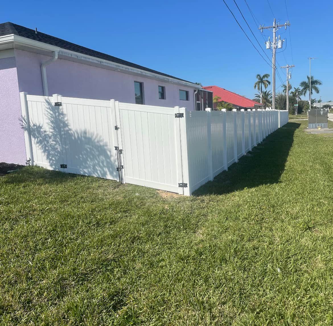 A white fence surrounds a lush green yard in front of a house.