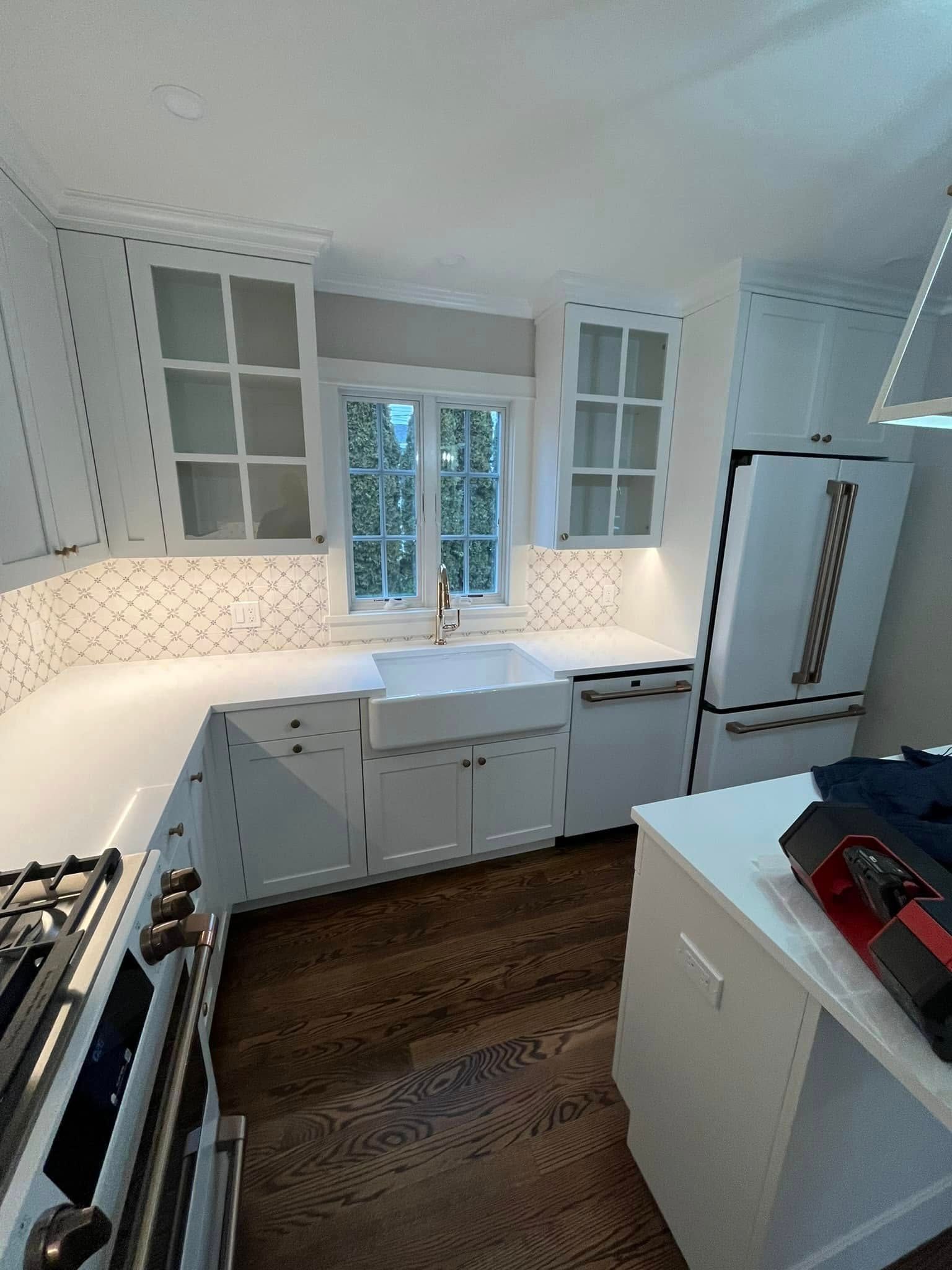 A kitchen with white cabinets , a stove , a refrigerator , a sink , and a window.