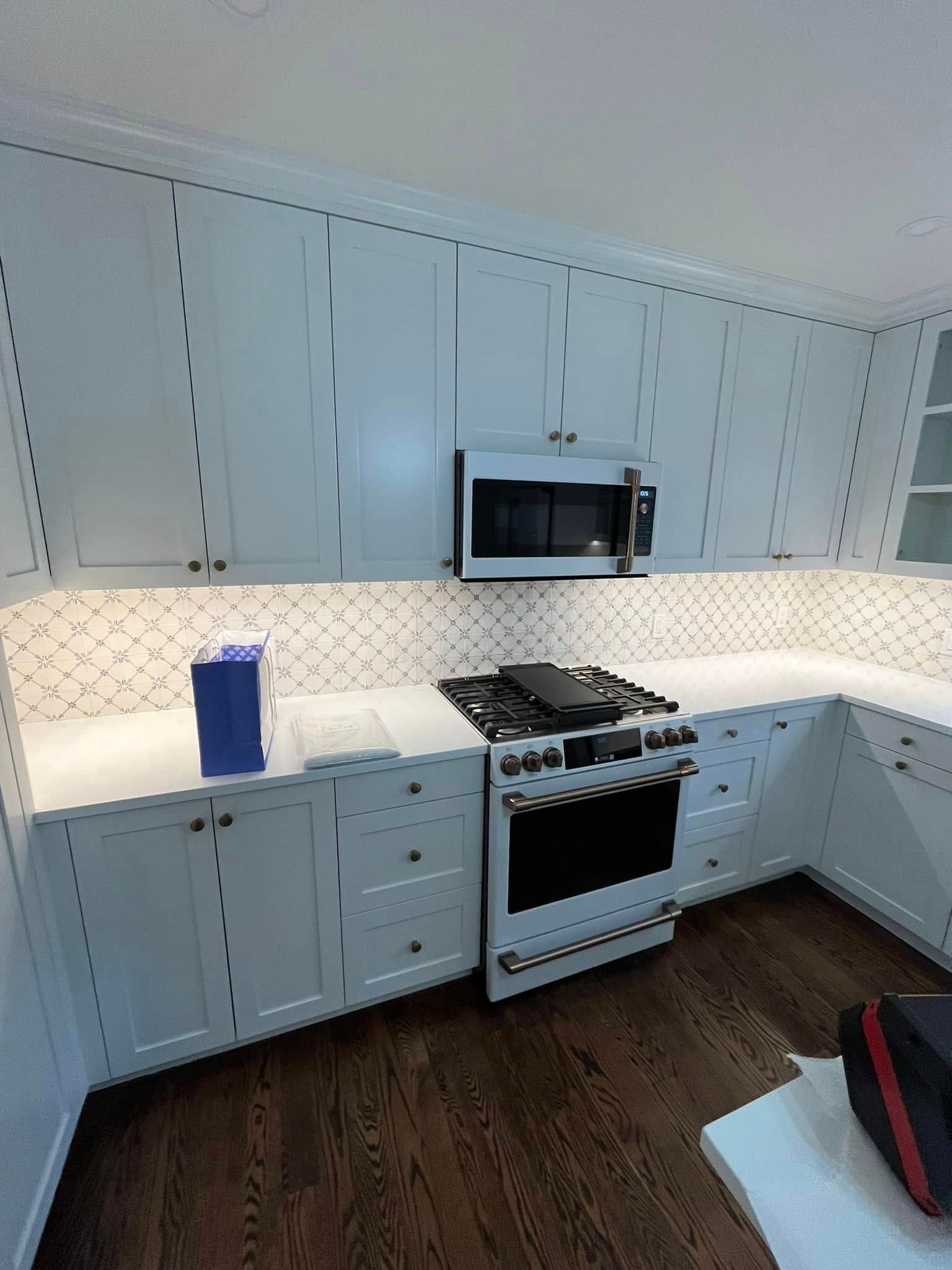 A kitchen with white cabinets , a stove and a microwave.