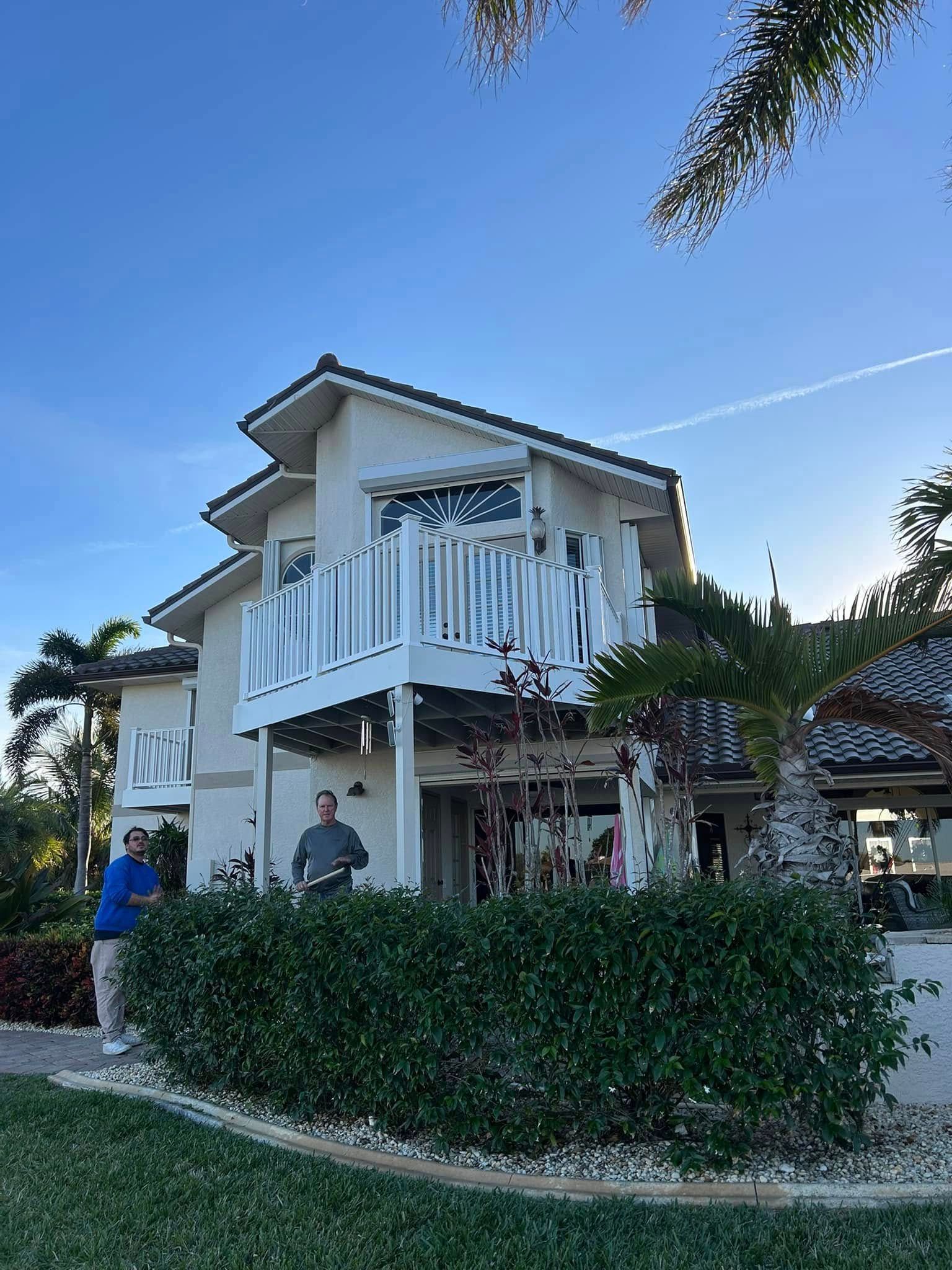 A man is standing in front of a large white house with a balcony.