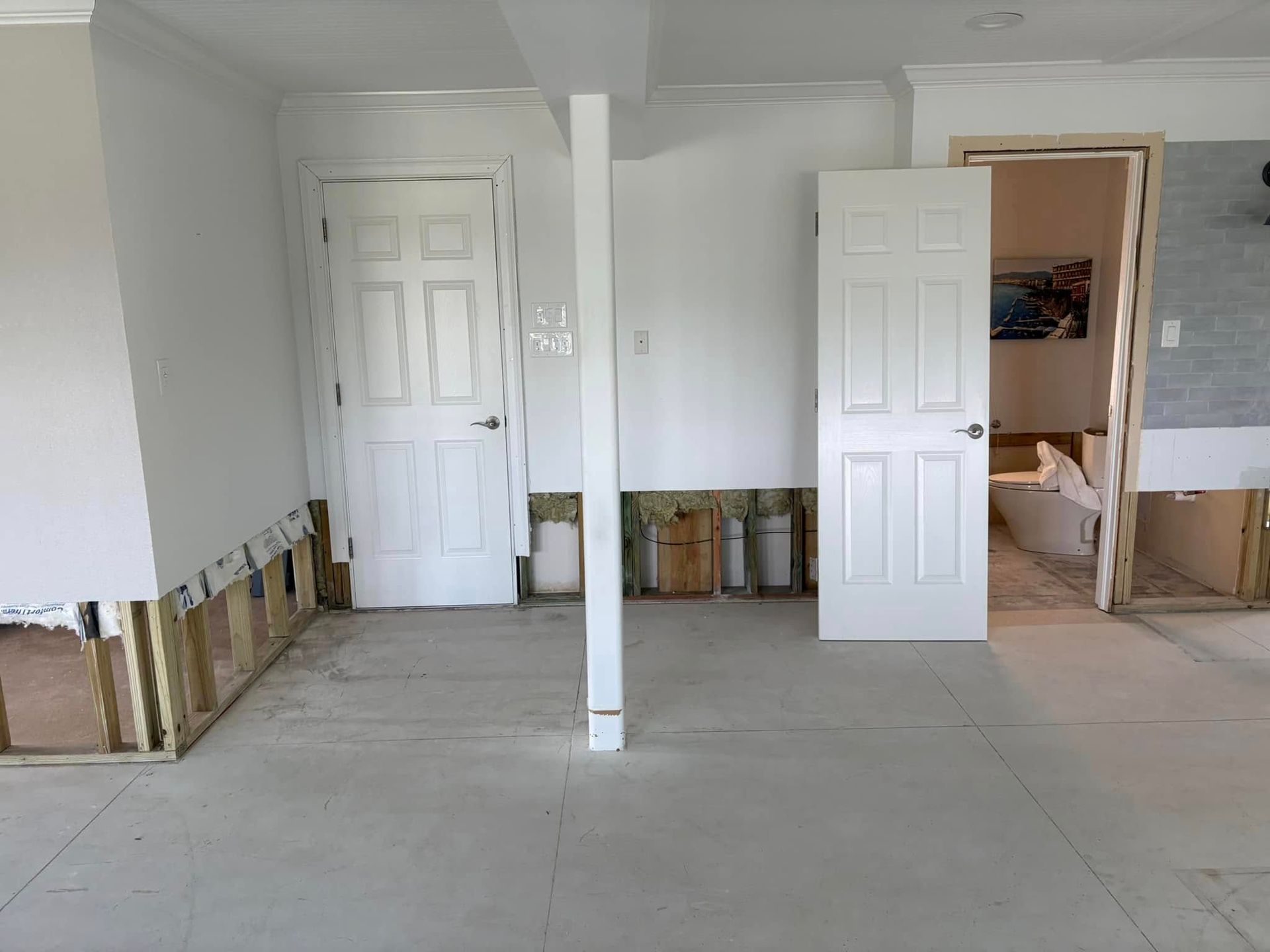 A room with two white doors and a bathroom in the background.