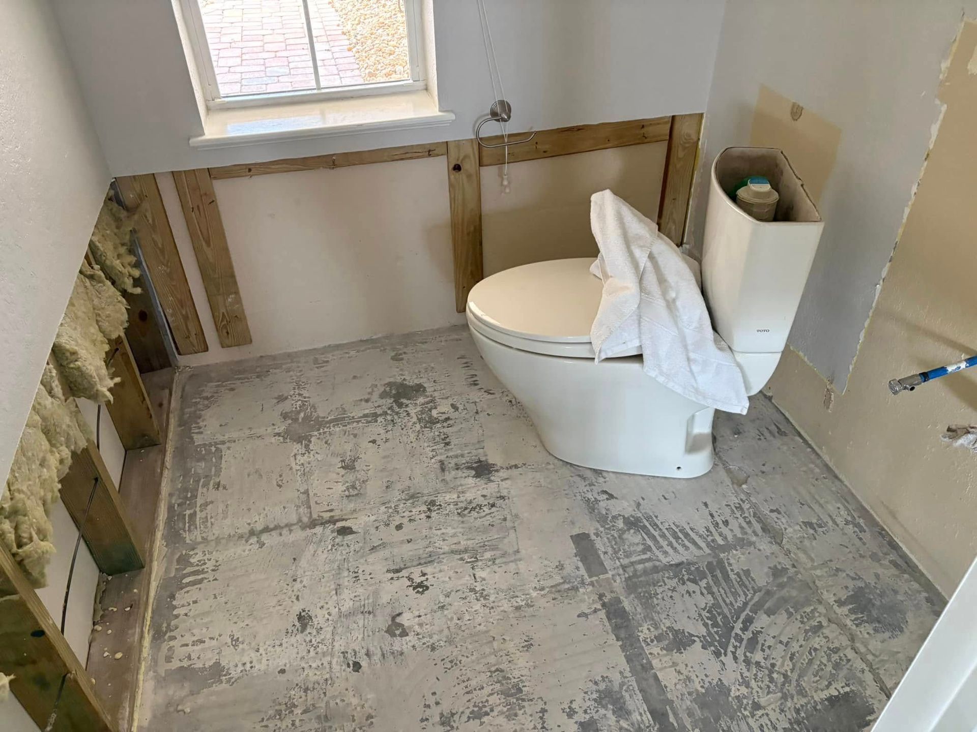 A toilet is sitting on a tiled floor in a bathroom under construction.