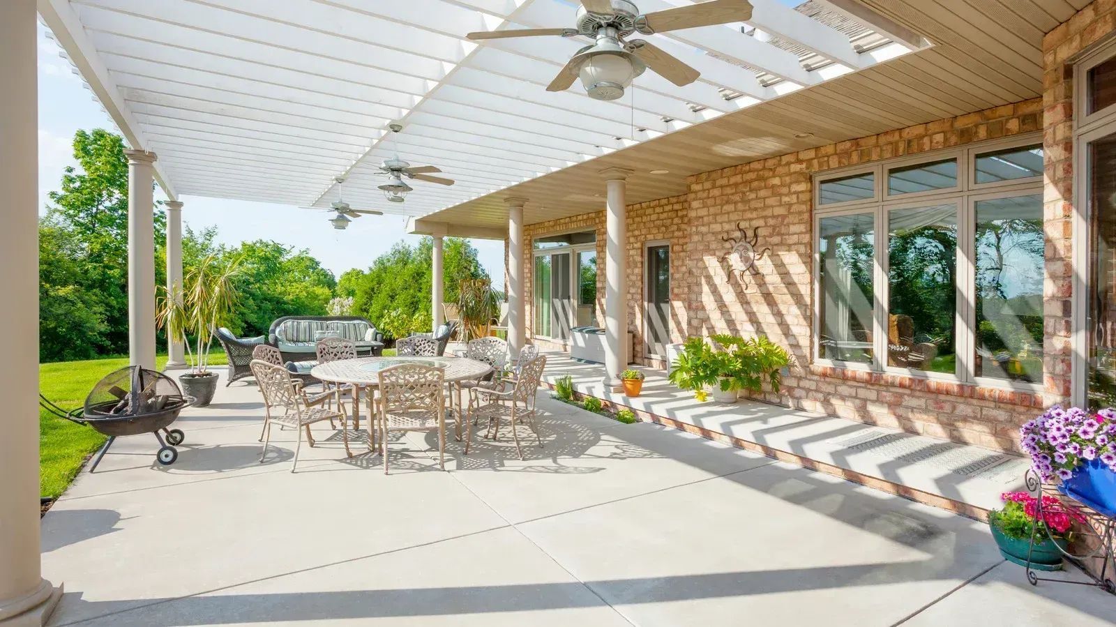 Patio with dining area, brick wall, and pergola. Includes outdoor furniture, potted plants, and ceiling fans.