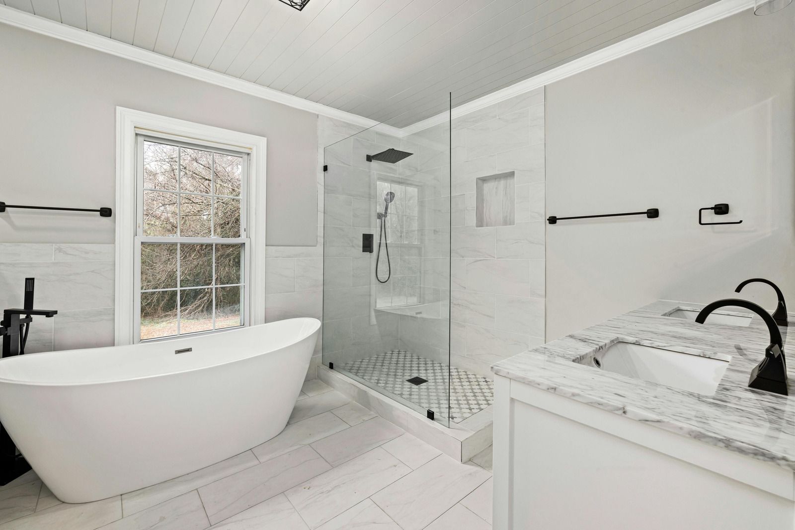 Bright white bathroom with freestanding tub, glass shower, marble vanity, and window.