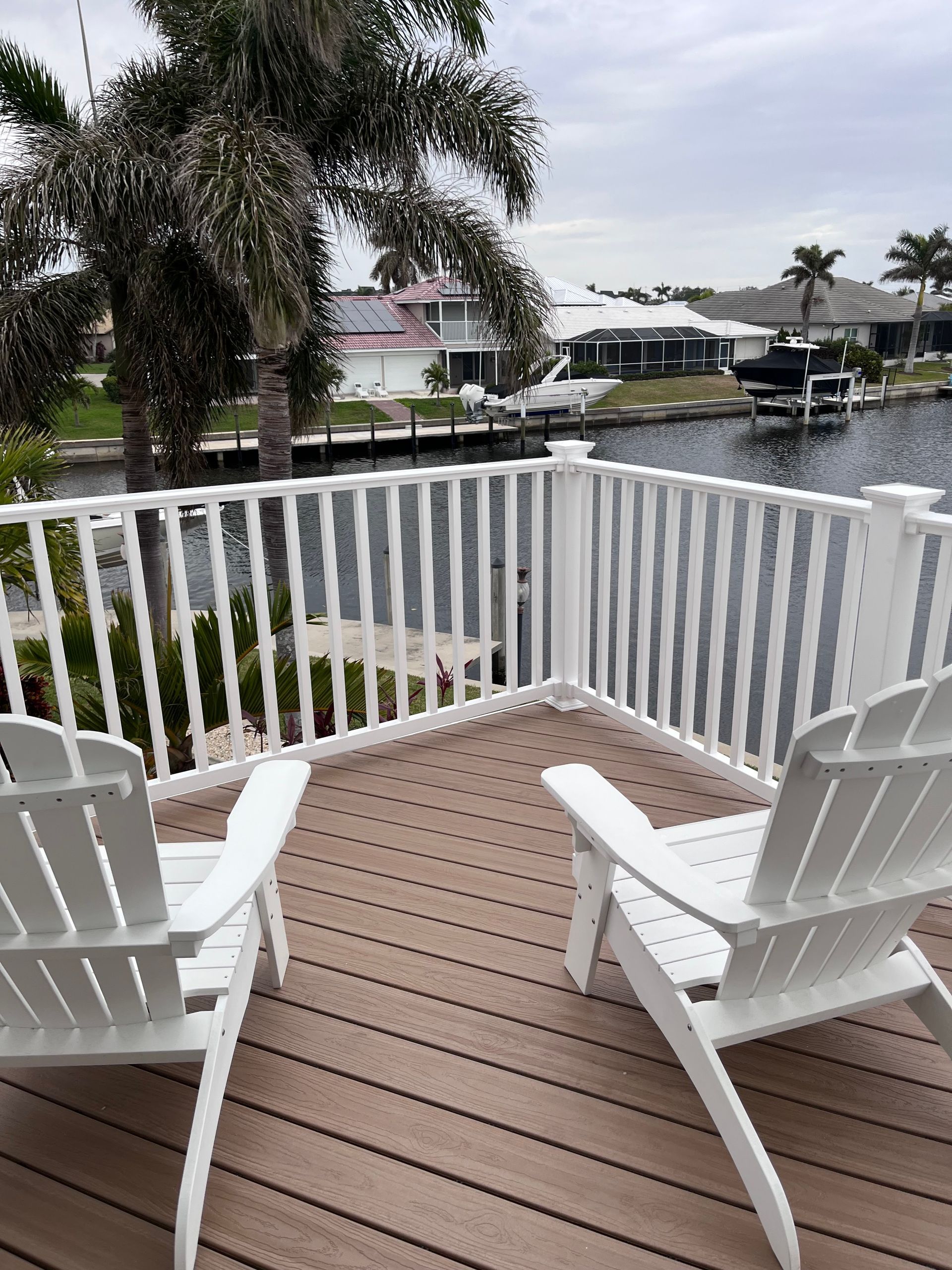 Two white chairs are sitting on a deck overlooking a body of water.