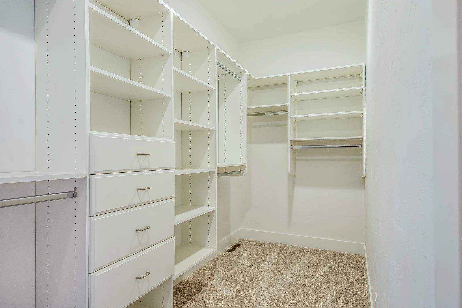 White walk-in closet with shelves, drawers, and hanging rods; carpeted floor.