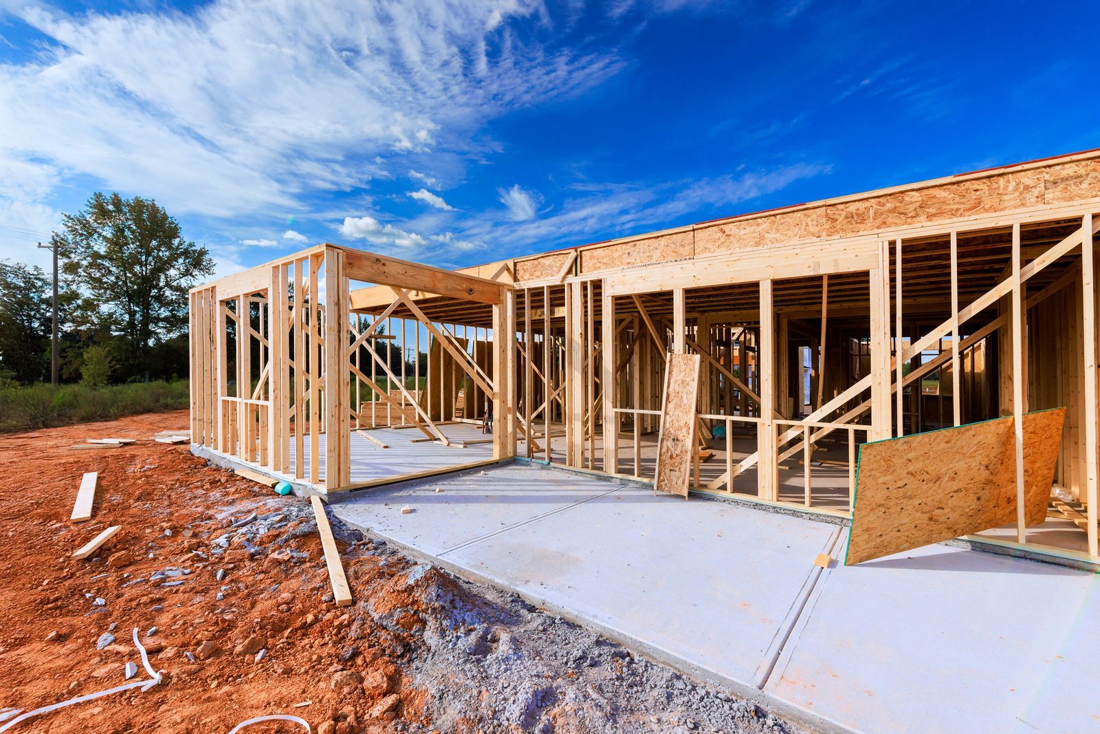 Construction of a house with wooden framing on a concrete foundation, set against a blue sky.