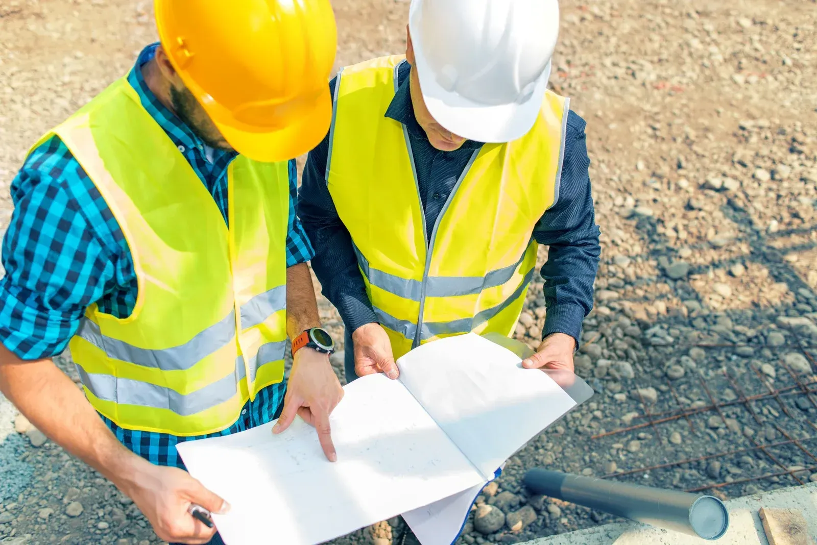 Two construction workers are looking at a blueprint on a construction site.