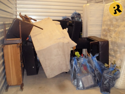 Storage unit filled with furniture and bags, including a sofa, mattress, and framed items.