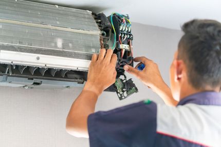 A man is fixing an air conditioner with a screwdriver.