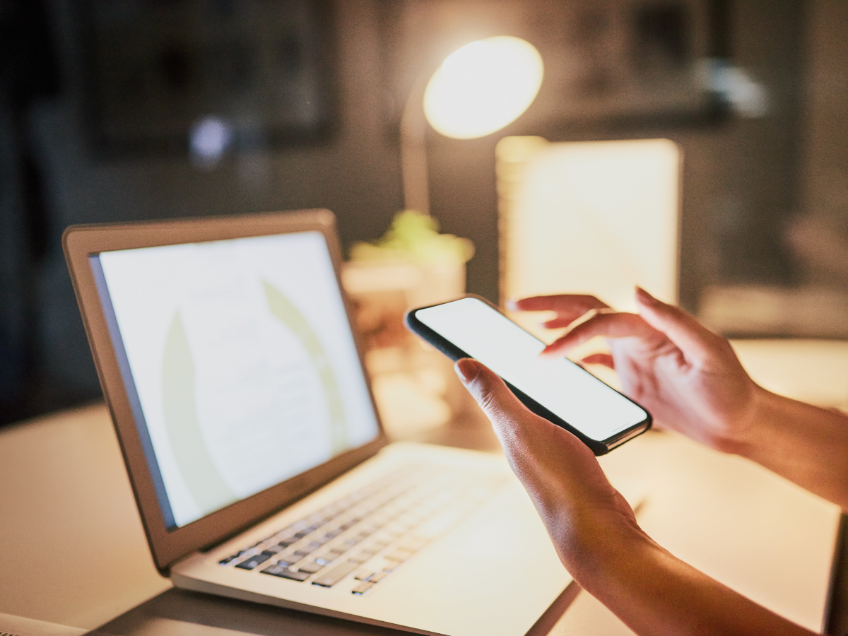 A person is using a cell phone in front of a laptop computer. A person is using a cell phone in front of a laptop computer.