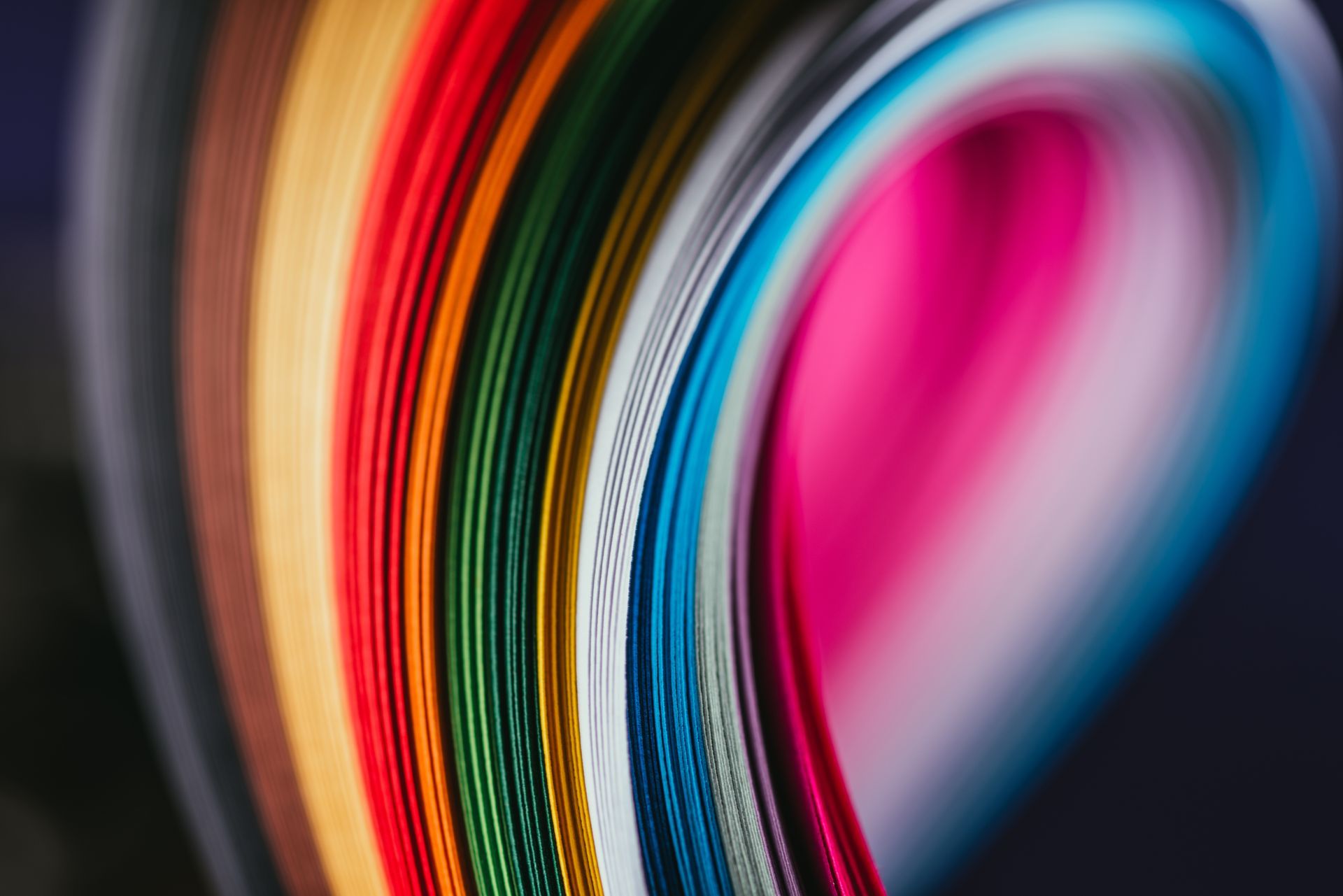 A close-up view of stacked, vibrant paper sheets curved into a colorful, rhythmic pattern.