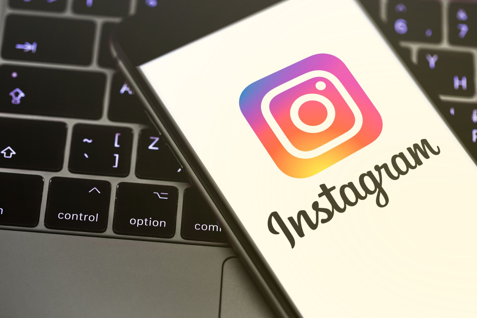 Instagram app logo on a smartphone, on a laptop keyboard. The logo is a gradient of colors.