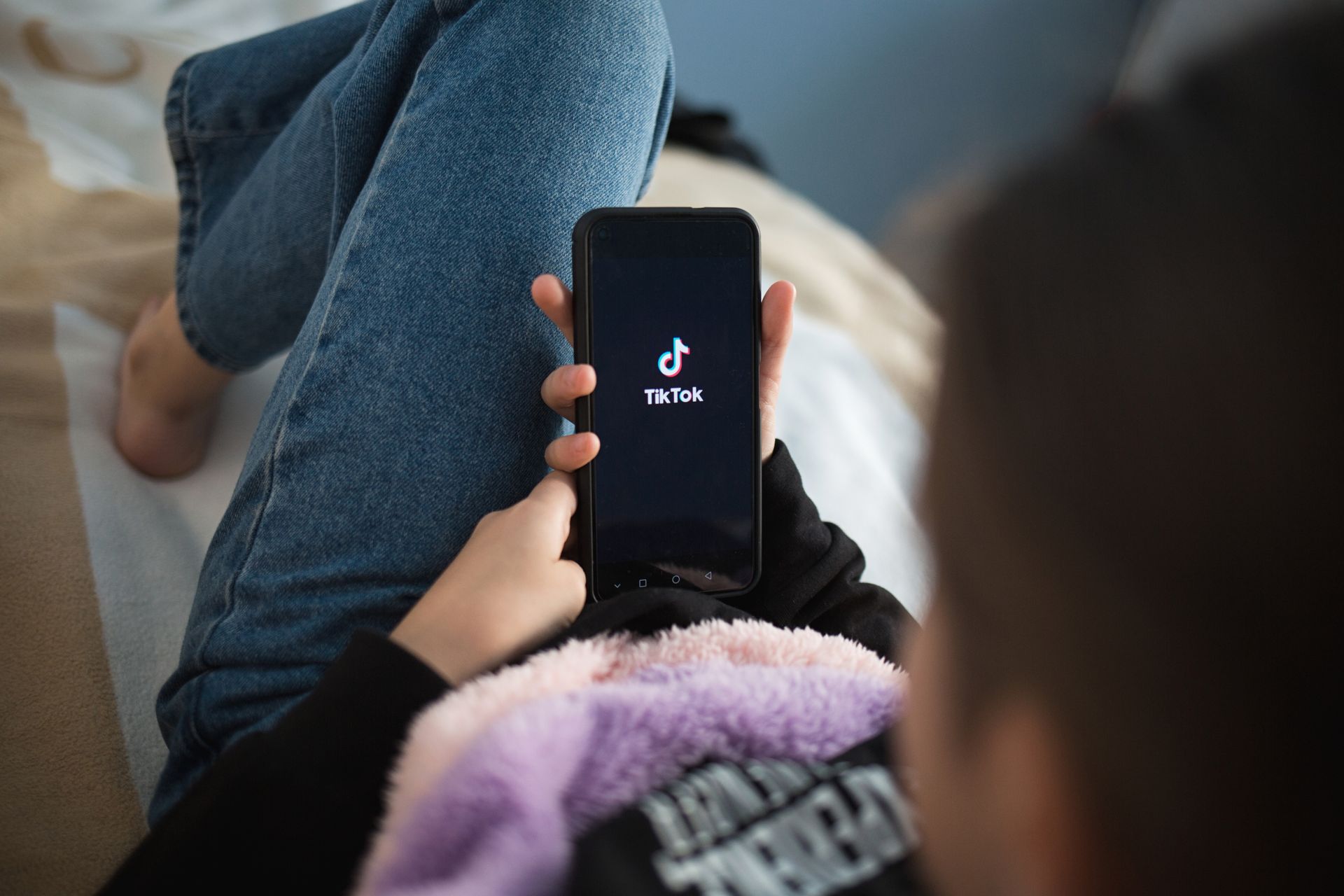Person holding a phone with TikTok app on screen. Laying down, wearing jeans.