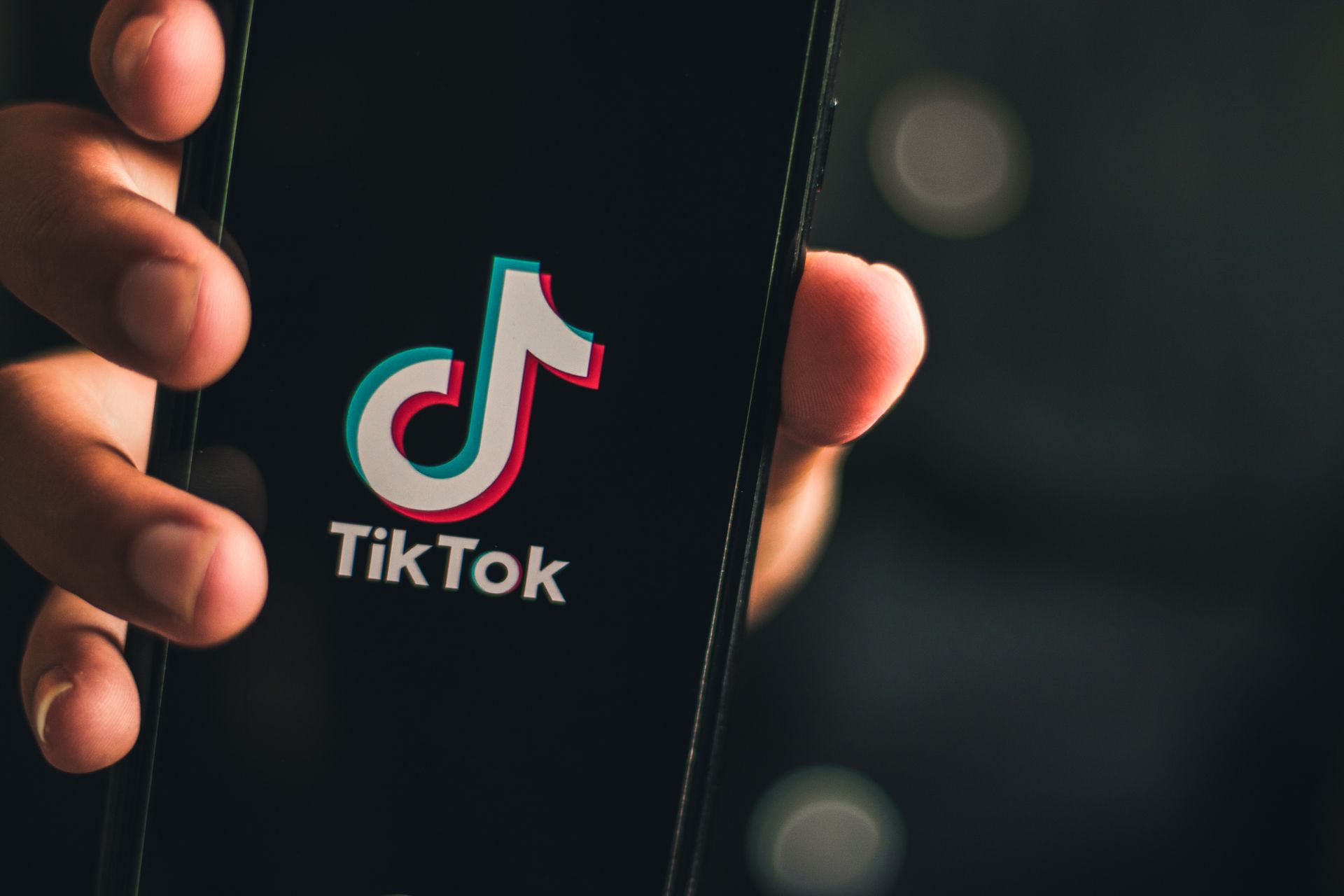 A hand holds a smartphone displaying the TikTok logo on a dark background.