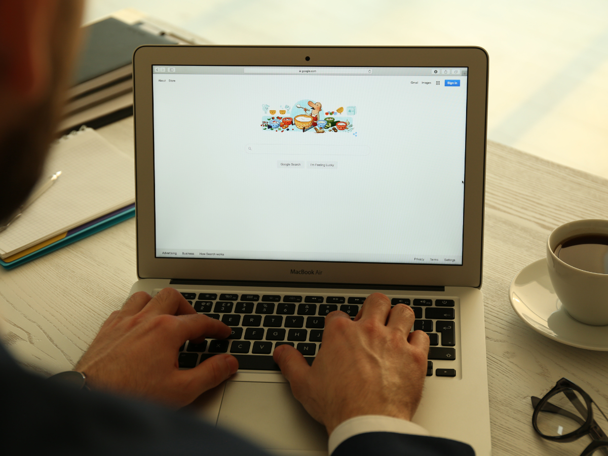 A man is typing on a laptop next to a cup of coffee